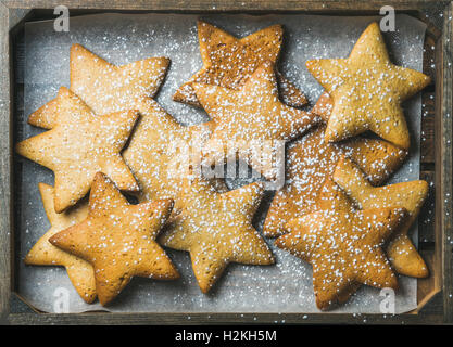 Sweet Christmas holiday gingerbread cookies in shape of stars with sugar powder on baking paper in rustic wooden tray, top view, Stock Photo