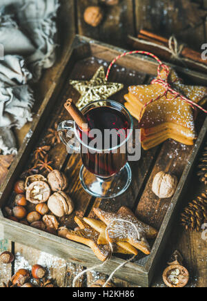 Glass of mulled wine in wooden tray with Christmas decoration toys, gingerbread cookies, nuts, cinnamon, anise and pine cones ov Stock Photo