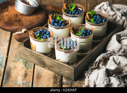 Homemade Tiramisu dessert in glasses with cinnamon, mint and fresh blueberry in wooden tray over rustic wooden background, selec Stock Photo