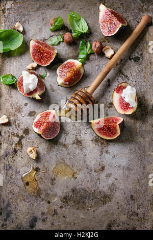 Fresh sliced figs with ricotta cheese, basil leaves, hazelnut and honey from honey dipper over dark rusty metal background. Spac Stock Photo