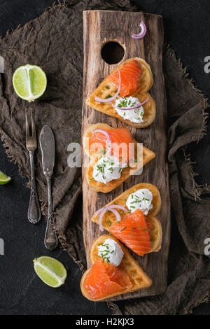 Wafers as heart shape with salted salmon, red onion, chive, lime and ricotta cheese on wooden cutting board with vintage cutlery Stock Photo