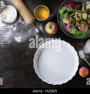 Ingredients for making apple cake. Flour, sugar, broken egg in tin cans, fresh apples with leaves in metal plate, white baking f Stock Photo