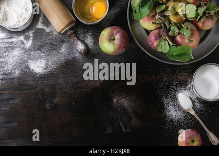 Ingredients for making apple cake. Flour, sugar, broken egg in tin cans, fresh apples with leaves in metal plate, vintage spoon Stock Photo