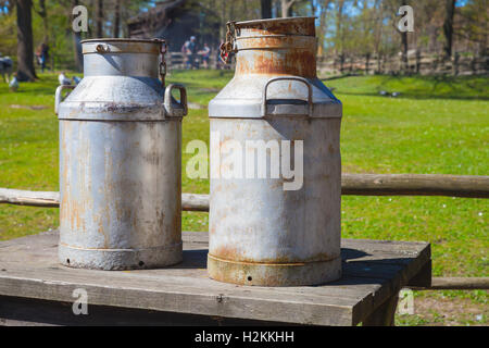 Two metal milk churns stand on wooden table over summer farm background Stock Photo