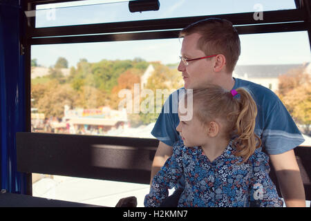 Beautiful men with his pretty happy daughter sitting in ferris wheel cabin at oktoberfest festival Stock Photo