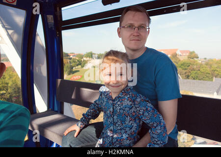 Beautiful men with his pretty happy daughter sitting in ferris wheel cabin at oktoberfest festival Stock Photo