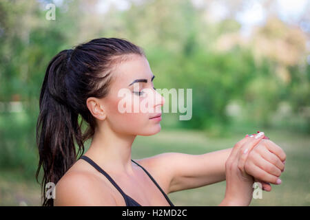 Young fitness girl checks stopwatch tracker on her wrist during running outdoor Stock Photo