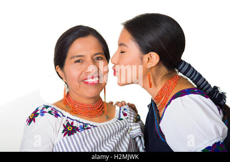 Beautiful hispanic mother and daughter wearing traditional andean clothing, young woman kissing her mom on cheek while posing happily, white studio background Stock Photo