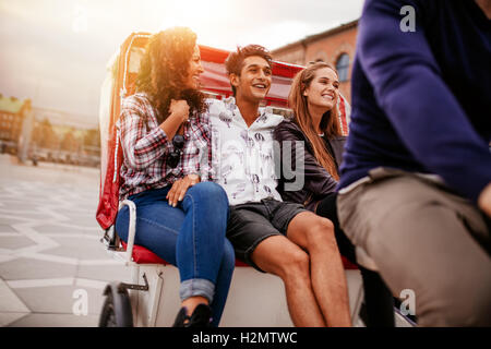 Group of young friends enjoying tricycle ride. Teenagers riding on tricycle on city road. Stock Photo