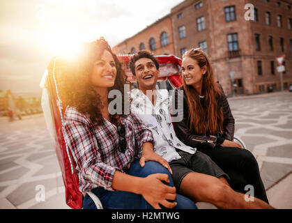 Three young people having fun on tricycle in the city. Young man and women riding on tricycle on road and smiling. Stock Photo