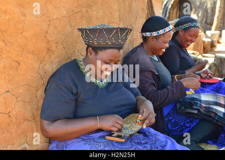 Zulu women making traditional beaded decorations at Shakaland Cultural Village, whilst seeking the shade from a rondavel, KwaZulu-Natal,South Africa