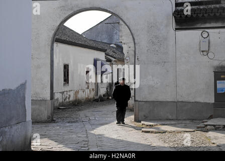 A local Chinese man wearing a cap and black clothes takes a stroll down the back streets of Tongli, a water town in China. Stock Photo