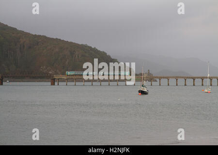 Arriva Trains Wales ATW service train crosses Barmouth Bridge, the Network Rail infrastructure wooden viaduct over the Mawddach estuary Cambrian Coast Stock Photo