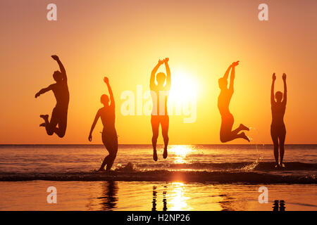 Group of happy people jumping in the sea at sunset, concept about having fun on the beach, silhouette