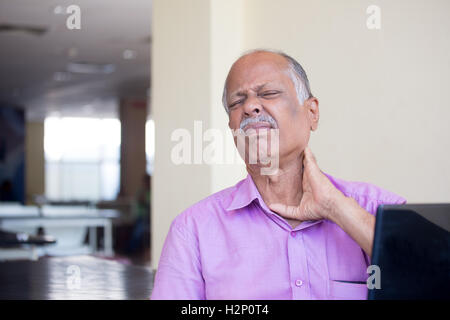 Closeup portrait, elderly gentleman in pink shirt with cramping neck pain after using black laptop all day, trying to soothe Stock Photo
