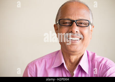 Closeup portrait, smart elderly man in pink shirt with dark eye glasses, specs, sitting down laughing, isolated indoors white Stock Photo