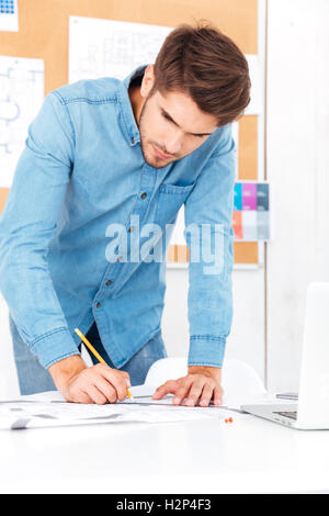 Concntrated young businessman making notes while standing at the office desk Stock Photo