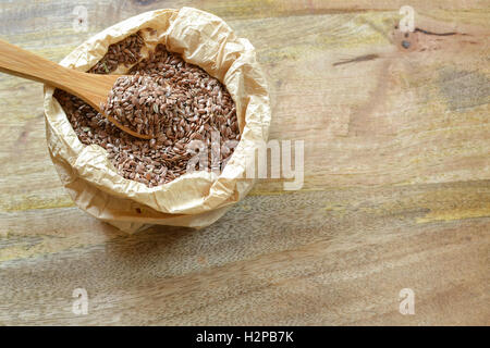 Wooden spoon picking up bunch of flax seeds from paper bag, on wooden background Stock Photo