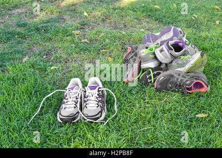 A pile of old running shoes beside a pair of new shoes. Stock Photo