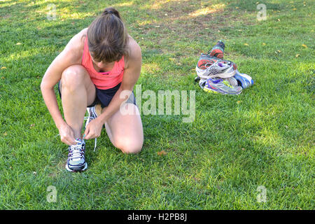 Middle-aged woman tying her running  shoes in front of a pile of old shoes Stock Photo