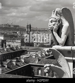 1950s, historical, a chimera on the Notre-Dame Cathedral above the city of Paris, France.  Unlike the famous gargoyles of Notre-Dame, the  grotesque limestone figures designed as spouts to convey rainwater away from the roof, these stone statues do not protrude from the external walls. Instead, they line the Galerie des Chimères, a balcony that connects the two bell towers. Peering over the balustrade, where they keep watch over the city below, they were a new addition to the Cathedral in the mid 1800s when it underwent restoration. 56 chimera or grotesques as they are known were erected. Stock Photo