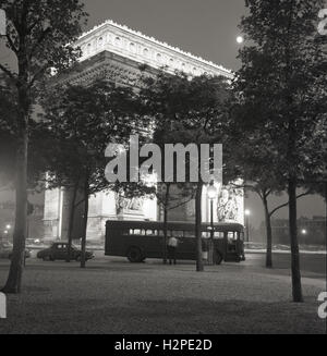 1950s, historical, Paris, France, evening time and a bus waits for passengers at the Place de l'Etoile, with the Arc de Triomphe, at the centre of the meeting point of of twelve straight avenues, lit up. Stock Photo