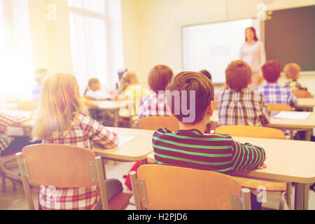 Rear view of group of kids studying while sitting on their desk at ...