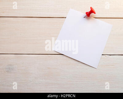 White square sheet of paper for notes pinned by red button to the white rough painted wooden wall Stock Photo