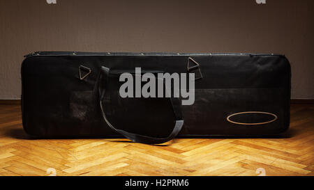 Old bass guitar suitcase, on parquet in front of a white wall. Stock Photo