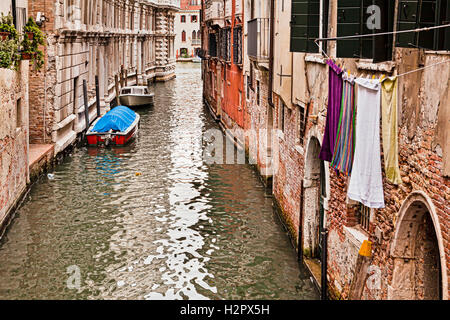 day to day life in Venice along small peripheral canal with old brick walls of aged building houses, windows and laundry Stock Photo