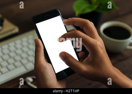 closeup hand use phone showing white screen on work desk, blank phone screen with clipping path easy for adjust app screen Stock Photo