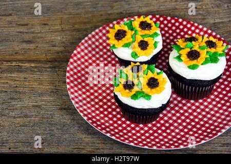 sunflower frosting design on chocolate cupcakes on red and white checkered plate Stock Photo