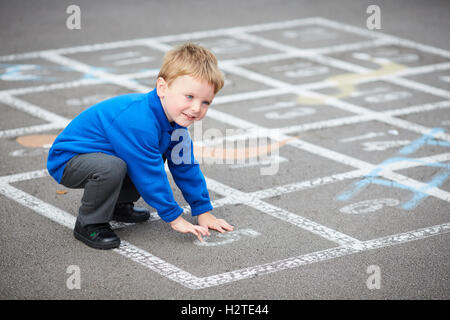 School boy child playground games  playing traditional chalk painted game snakes ladders uniform blue smart toddler Education ed Stock Photo