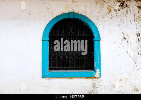 Detail of wall with old window painted blue handworked iron bars Stock Photo