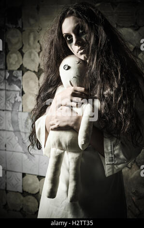 Horror style shot: a strange sad girl with moppet doll in hands Stock Photo