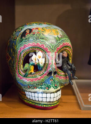 An ornately decorated skull. Lily flowers grow out of one eye socket and a monkey climbs out of another. Stock Photo