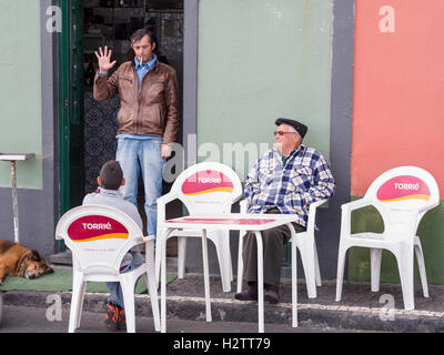 High Fives -- cafe scene. A man, smoking in a doorway gives a high five salute to a boy in a cafe chair.  An older man looks on Stock Photo