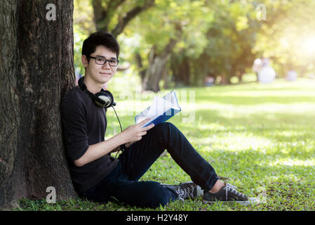 Asian young handsome man student reading book in nature. One student. Stock Photo