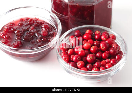 Lingonberries and lingonberry jam in glass bowls over white. Fresh red fruits of Vaccinium vitis-idaea, also mountain cranberry. Stock Photo