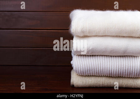 Stack of white and cozy knitted sweaters on rustic wooden background Stock Photo