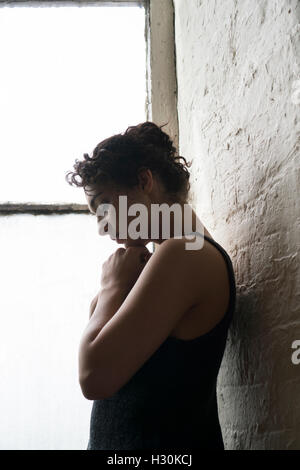 Sad young woman standing by the window Stock Photo