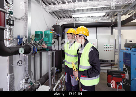 Two workers in hardhats at plant checking parameters of pressure Stock Photo