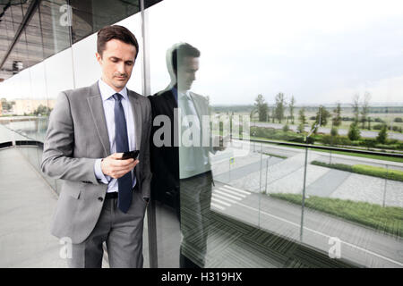 Handsome business man using a cell phone outdoors on the balcone of office building Stock Photo