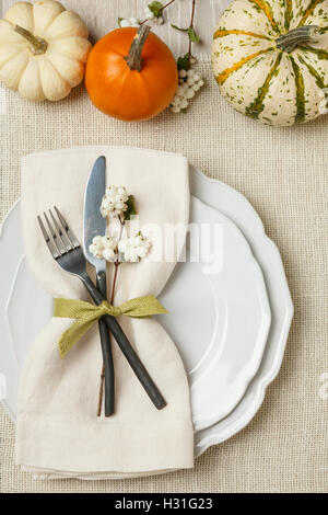 Fall autumn festive Thanksgiving dinner table place setting with miniature pumpkins, plate, fork, knife and napkin on burlap background Stock Photo