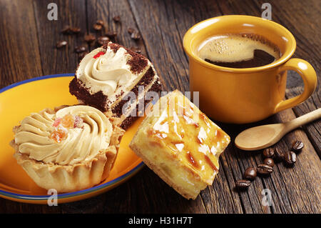 Three cakes in yellow plate and coffee cup on old wooden table Stock Photo