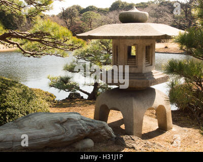 ishidoro stone lantern by pond with rock & tree,  Shinjuku Gyoen traditional japanese garden, tokyo, japan Stock Photo