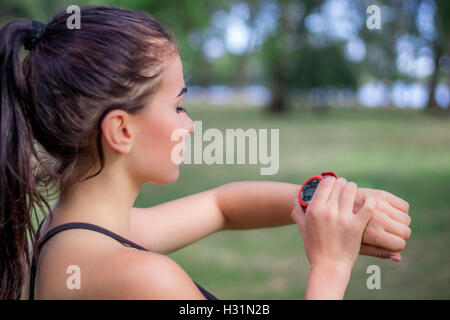 Young fitness girl checks stopwatch tracker on her wrist during running outdoor Stock Photo