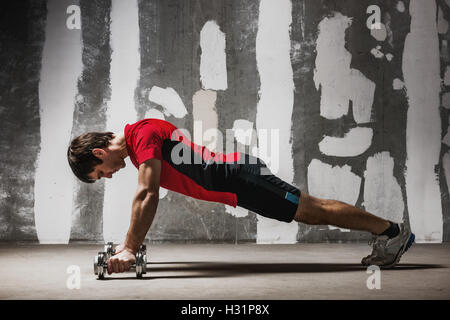 Man doing push ups on dumbbells  the wall backdrop Stock Photo