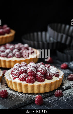 Delicious raspberry mini tarts (tartlets) with whipped cream on dark background Stock Photo