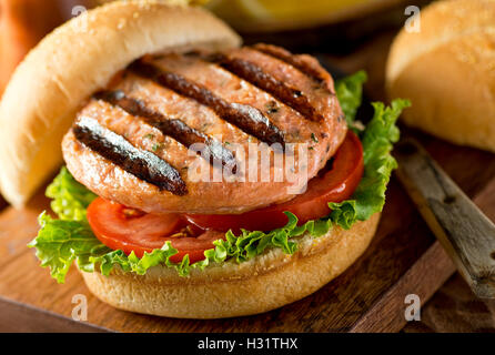 A delicious homemade grilled salmon burger with tomato and lettuce on a bun.